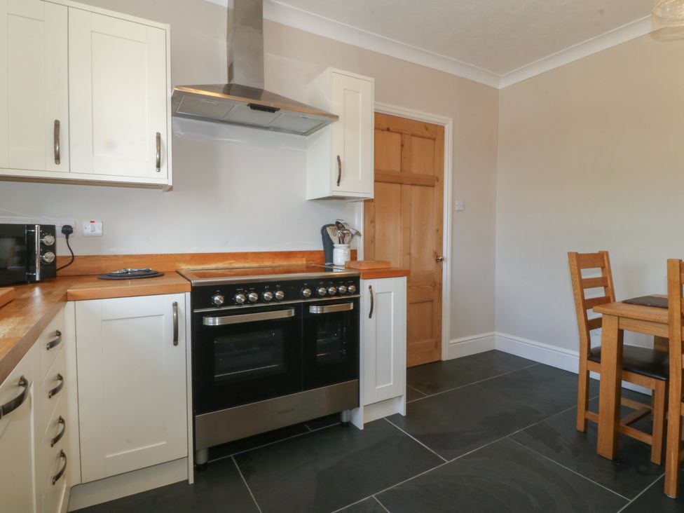 A kitchen with a stove oven microwave wooden cabinets and a wooden dining table and chairs at Glasfryn in Llandwrog