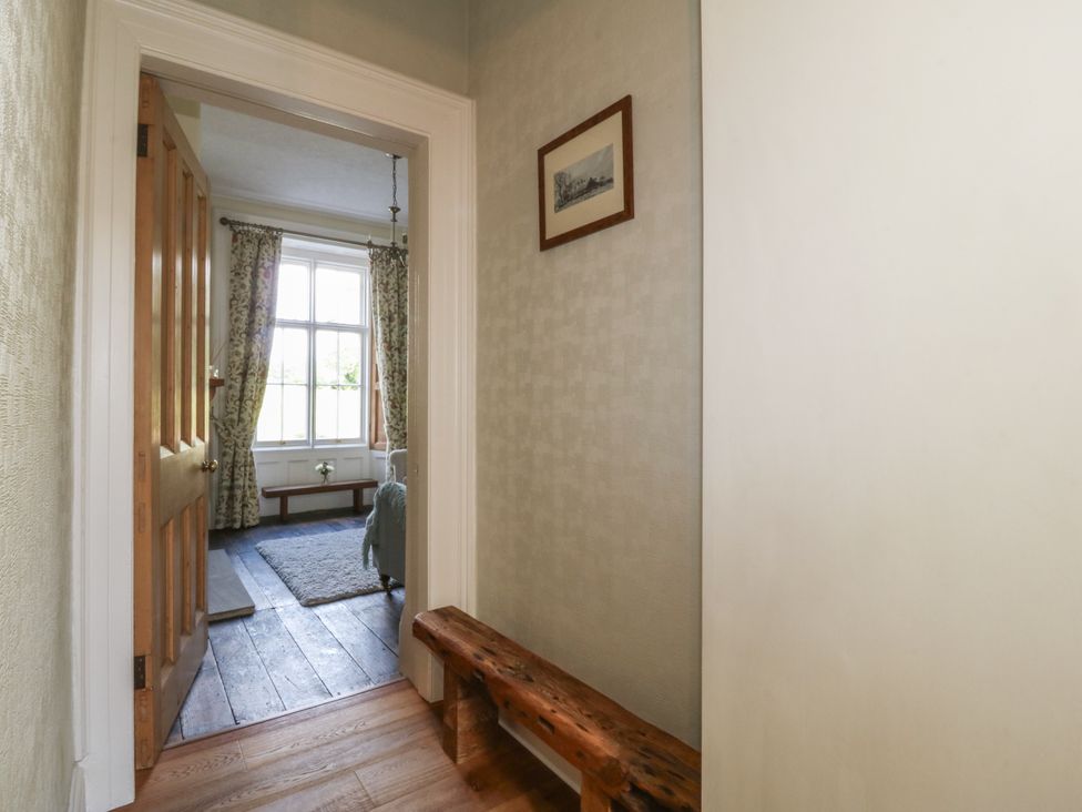 A hallway with a wooden bench and framed picture leading to a room with a window and curtains at Glasfryn in Llandwrog