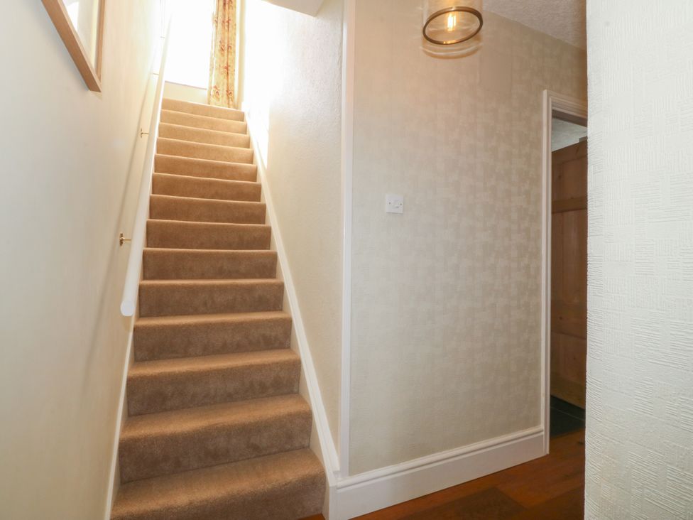 A carpeted staircase with a handrail and a light fixture in a hallway at Glasfryn in Llandwrog