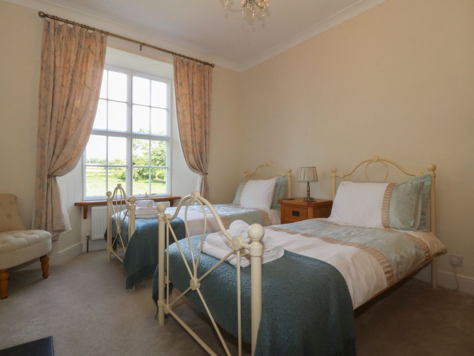 A bedroom with two single beds a bedside table with a lamp a window with curtains and a chair at Glasfryn in Llandwrog