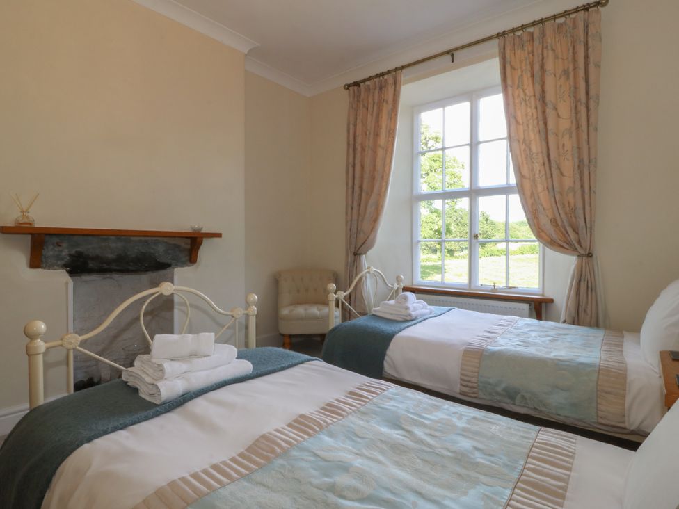 A bedroom with two single beds next to a window with curtains and a small armchair at Glasfryn in Llandwrog
