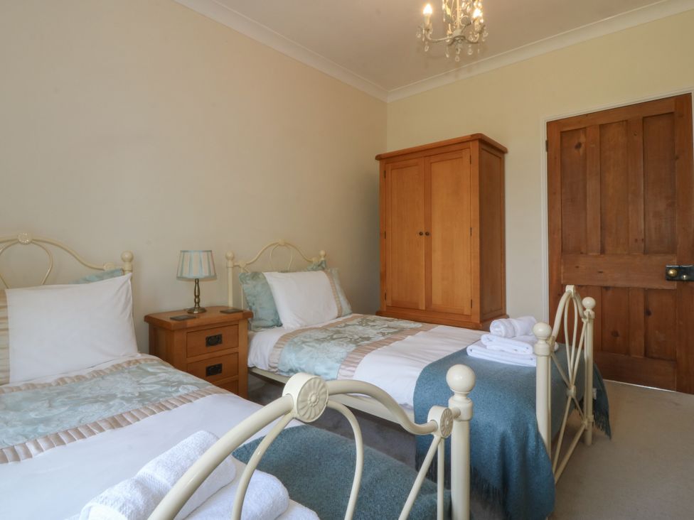 A bedroom with two single beds a wooden wardrobe and a wooden door at Glasfryn in Llandwrog