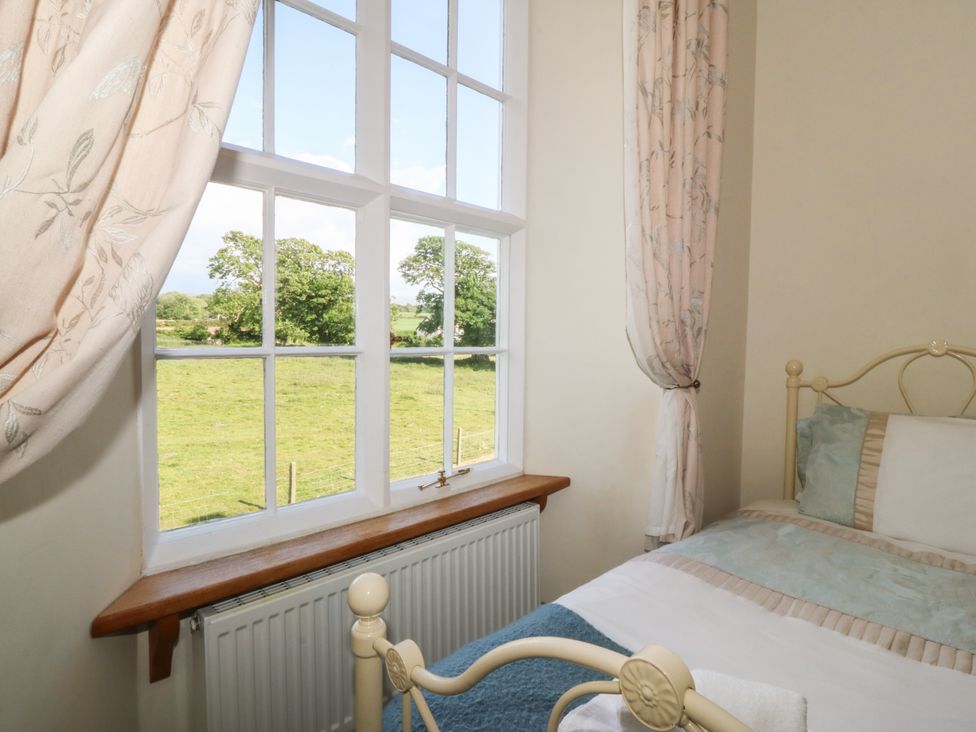 A bedroom with a metal bed near a window showing a green field at Glasfryn in Llandwrog