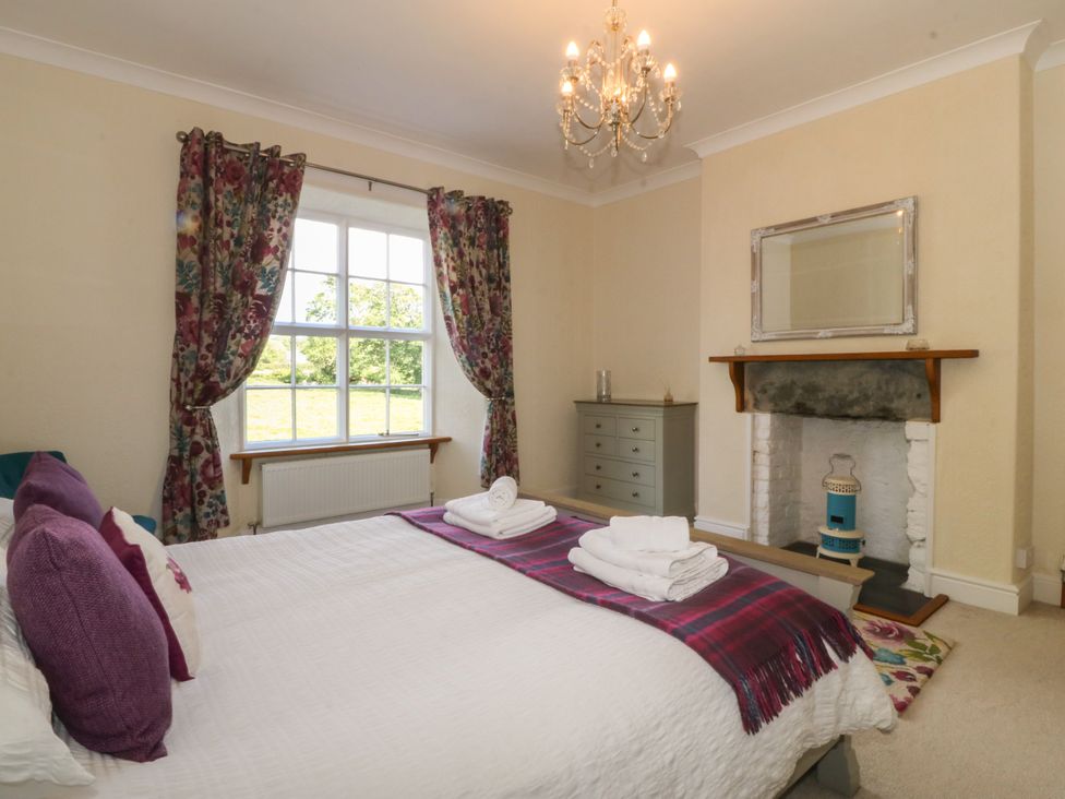 A bedroom with a bed, floral curtains on a window, a chest of drawers, and a fireplace at Glasfryn in Llandwrog