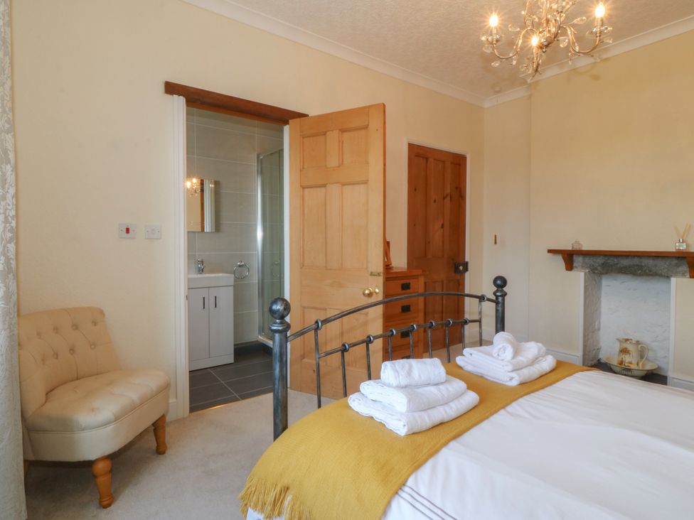A bedroom with a metal bed frame towels on the bed a beige chair and an open door leading to a bathroom at Glasfryn in Llandwrog