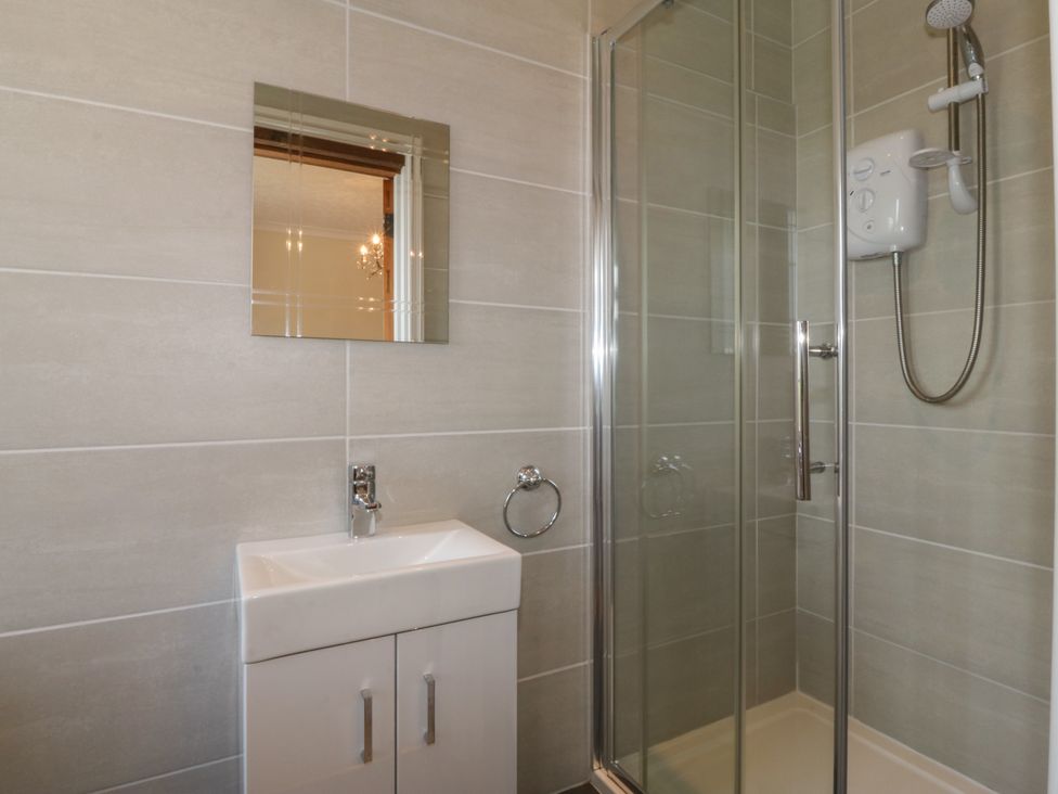 A bathroom with a small sink and cabinet a shower with a glass door and wall-mounted shower unit at Glasfryn in Llandwrog