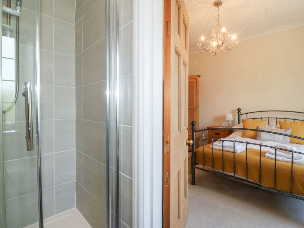 A bedroom with a metal bed frame and pillows next to an open door leading to a tiled shower area at Glasfryn in Llandwrog
