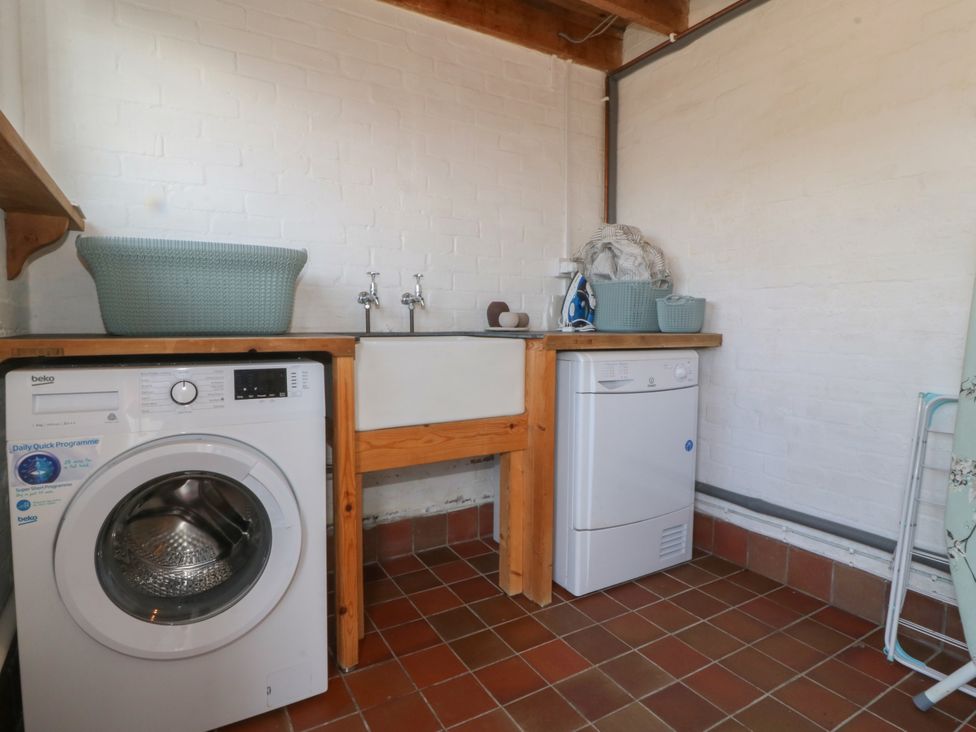 A laundry room with a washing machine dryer a sink and laundry baskets at Glasfryn in Llandwrog