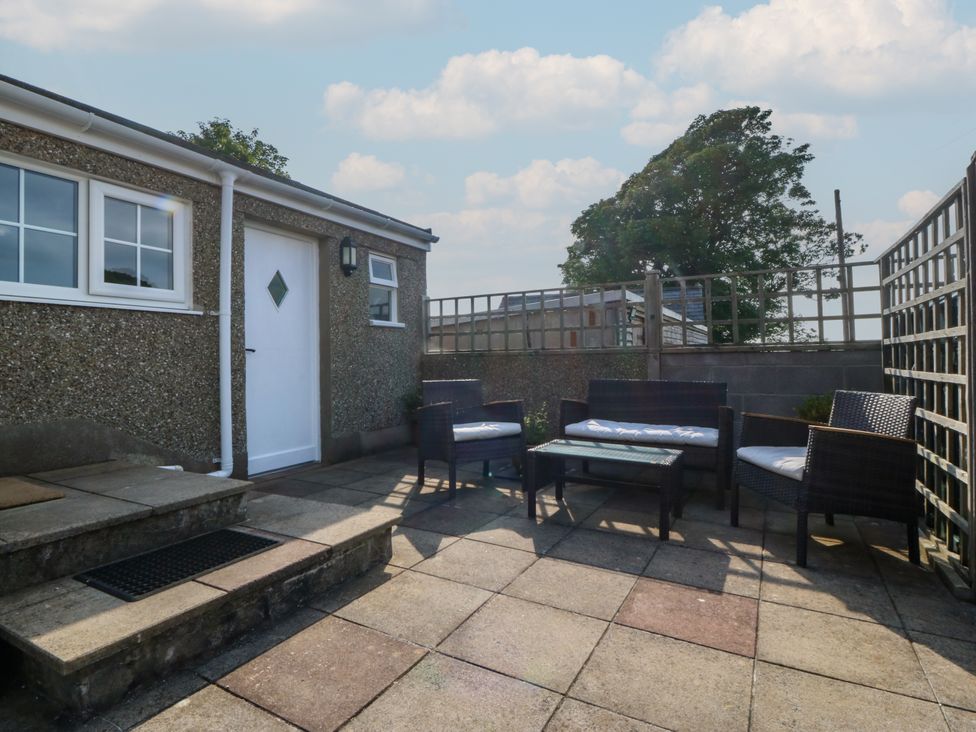 A paved outdoor patio with a white door and windows with wicker chairs and a table at Glasfryn in Llandwrog