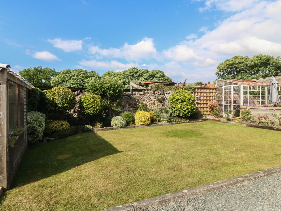 A garden with grass lawn bushes and trees next to a stone wall and a greenhouse at Glasfryn in Llandwrog