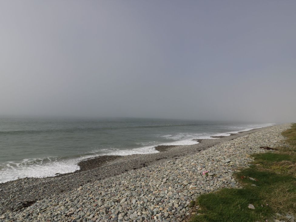 A beach with pebbles and grass by the ocean at Glasfryn in Llandwrog