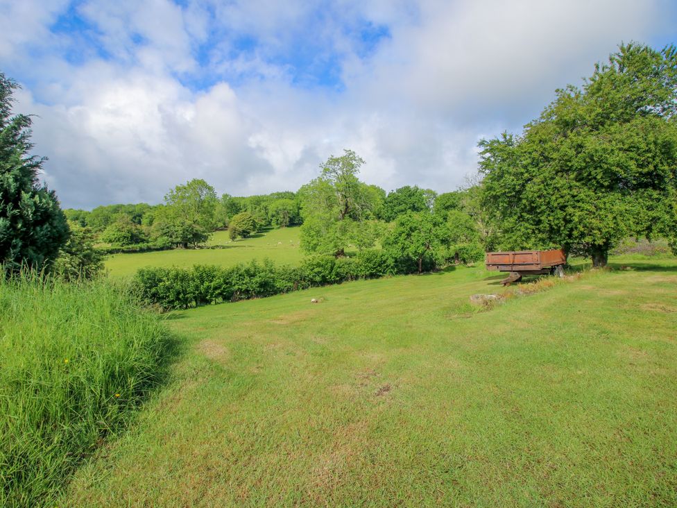 A garden with a bench under trees at The Long House Near Trefonen