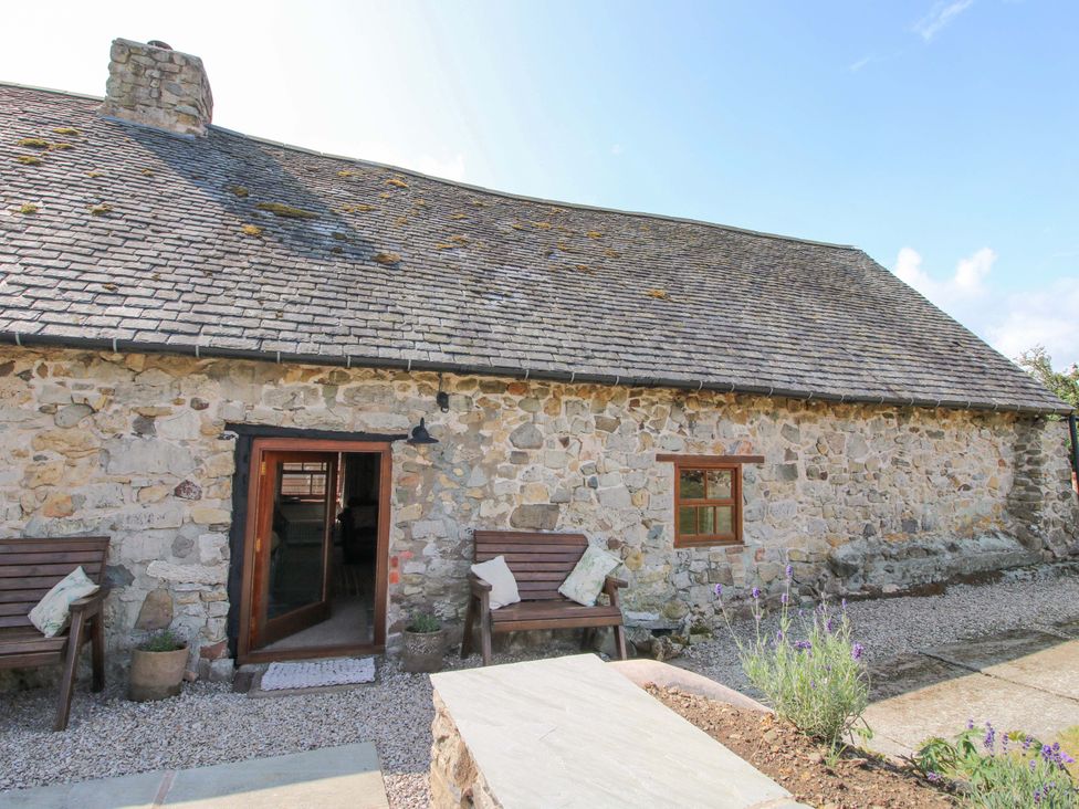 A stone house with wooden benches and gravel path at The Long House Near Trefonen