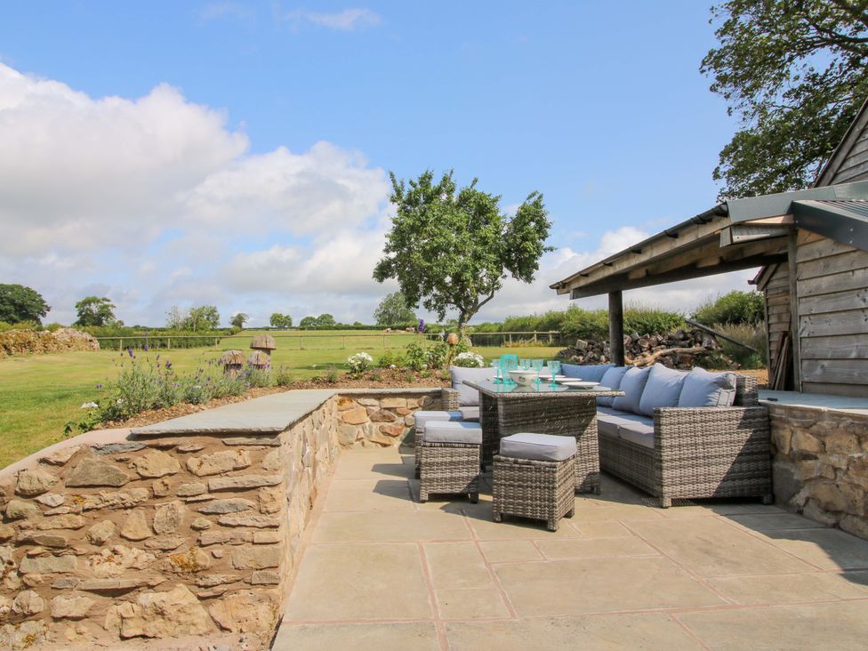 A garden with outdoor furniture and a stone wall at The Long House Near Trefonen