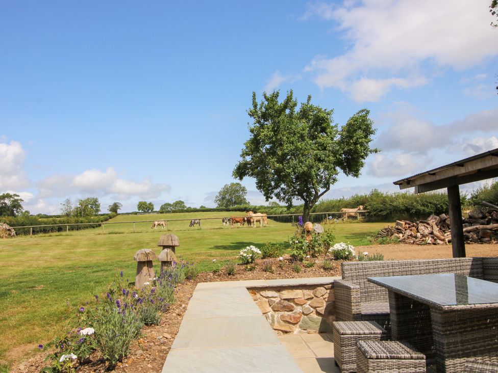 An outdoor seating area with a table and chairs overlooking a field with cows at The Long House Near Trefonen
