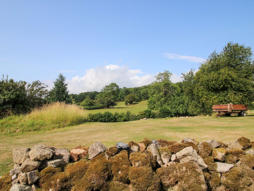A landscape view with grass, trees, and a trailer at The Long House near Trefonen