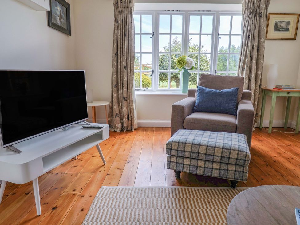 A living room with a television and armchair at Tithe Barn Cottage in Litton Cheney near Burton Bradstock