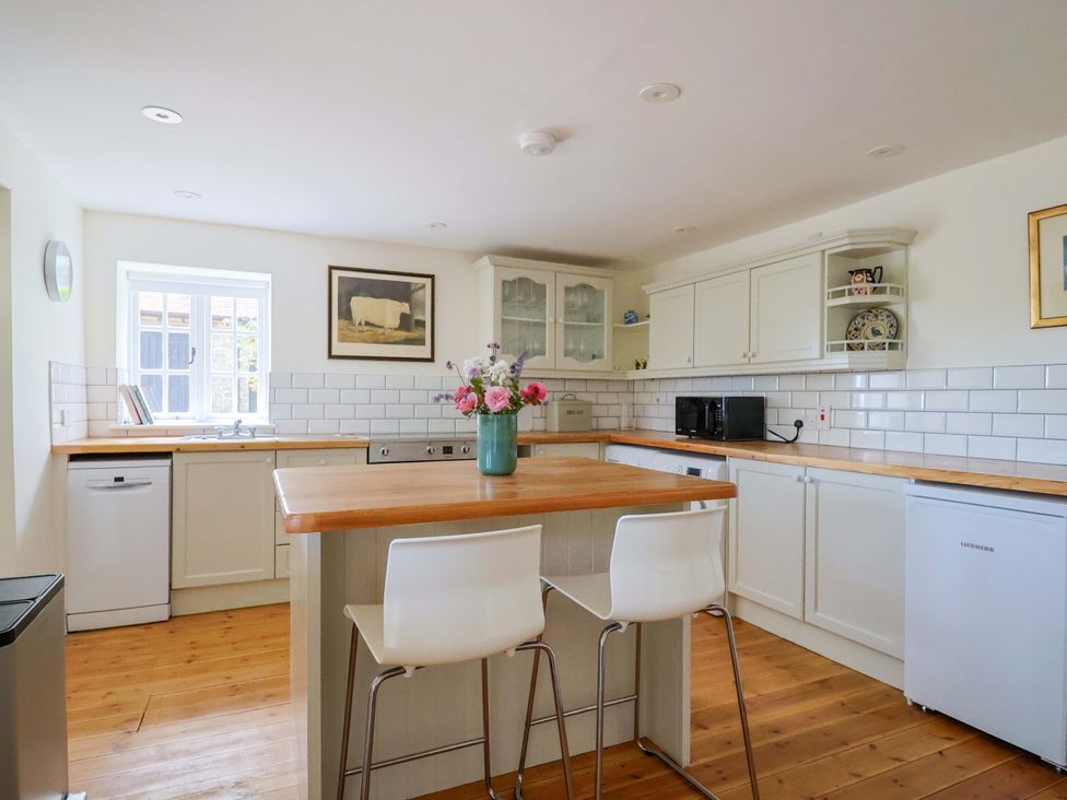A kitchen with a sink, refrigerator, and bar stools at Tithe Barn Cottage in Litton Cheney near Burton Bradstock
