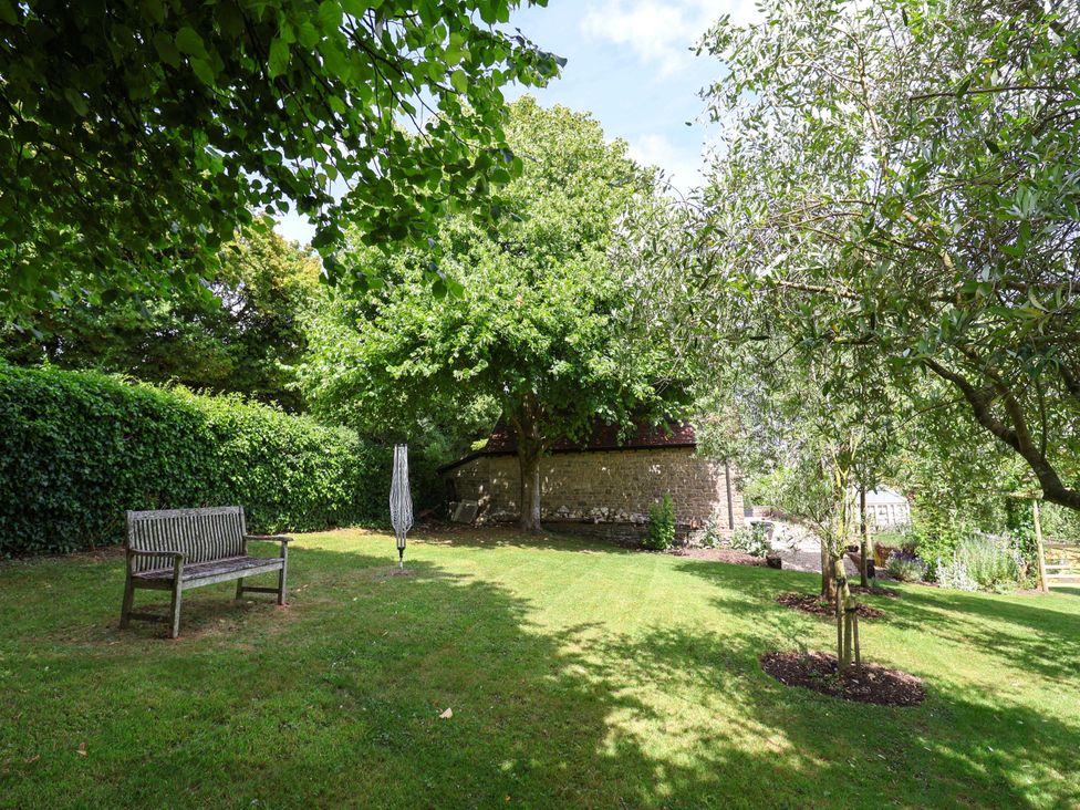 A garden with a bench and trees at Tithe Barn Cottage in Litton Cheney near Burton Bradstock