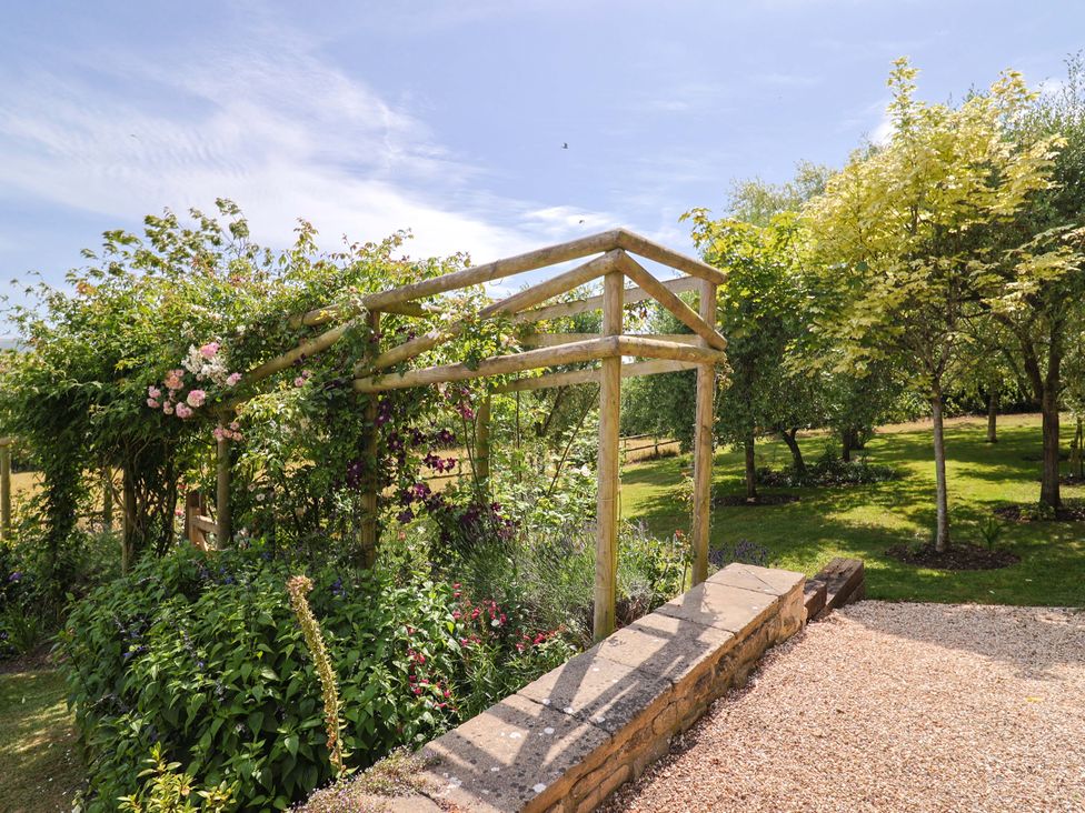 A garden with a wooden pergola and flower beds at Tithe Barn Cottage in Litton Cheney near Burton Bradstock