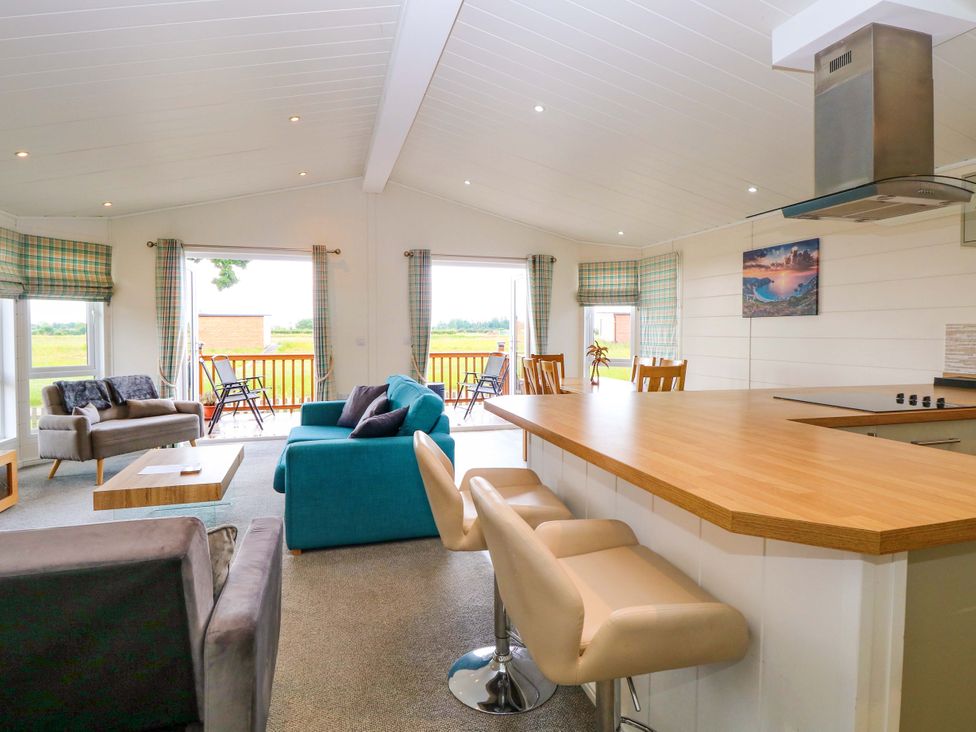 A living room with a sofa, chairs, and kitchen counter at Oak Tree Holiday Lodge in Stonham Aspal