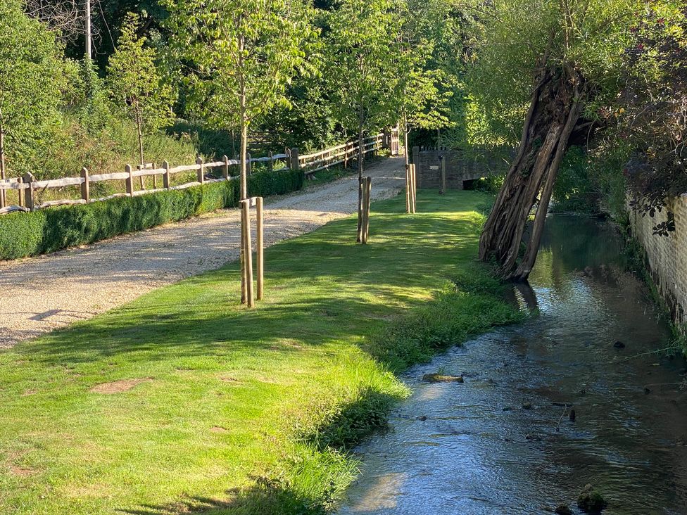 A gravel path along a stream with trees and a fence at The Annexe, Cleveley Mill in Chipping Norton