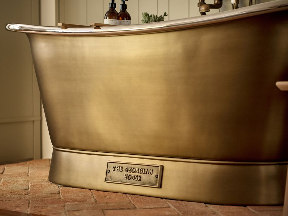 A bathtub with soap dispensers and a plant at Stretton Hills Peaks - The Georgian House, Ludlow