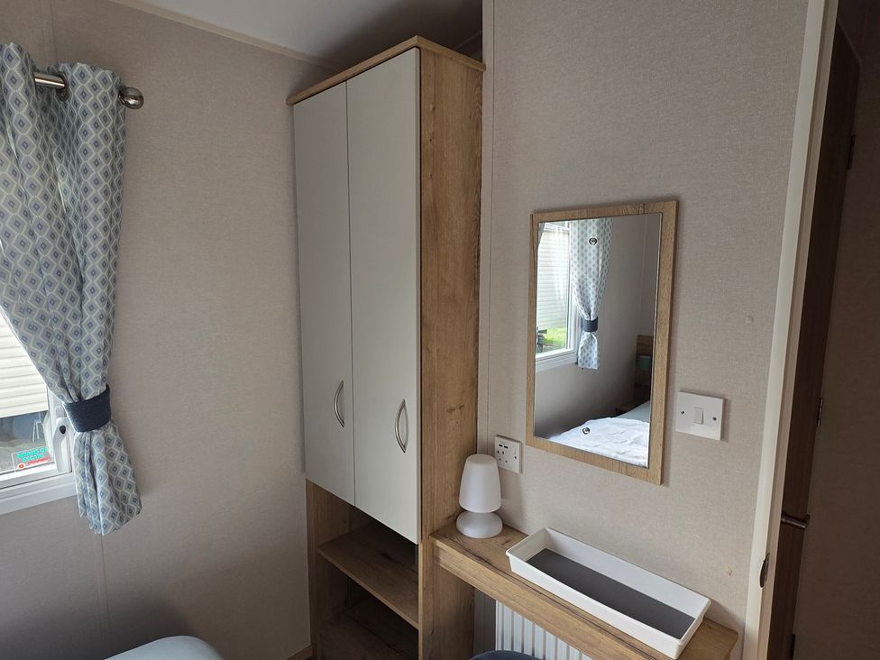 A bedroom with a cabinet, mirror, lamp, and shelf at Pines 15 in Porthcawl