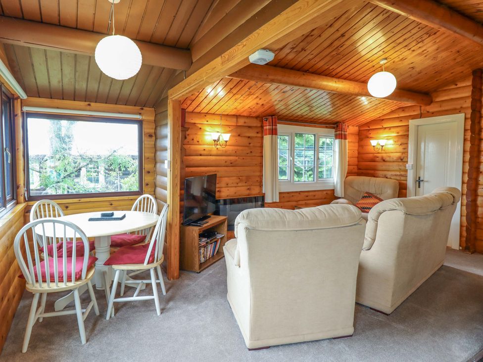A living room with a sofa, table, and television at Y Bwthyn Pren, Cabin 209, Trawsfynydd