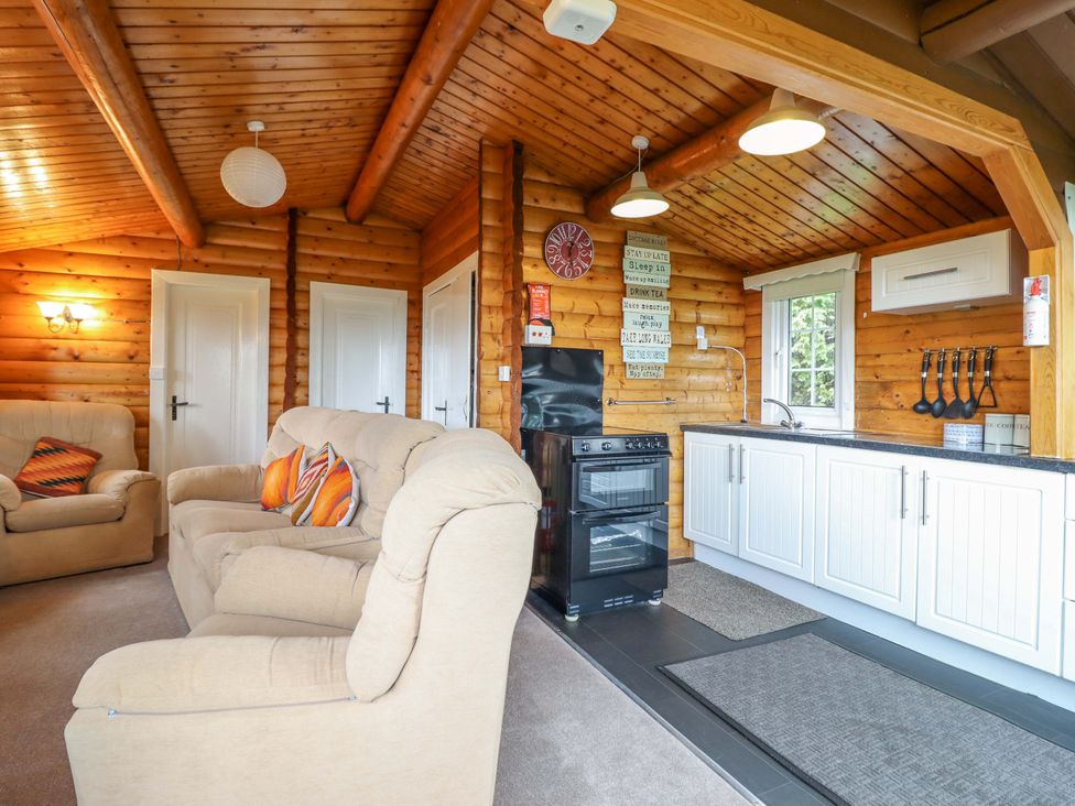 A living room with a sofa and kitchen area at Y Bwthyn Pren, Cabin 209, Trawsfynydd
