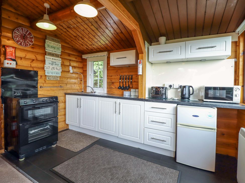A kitchen with a stove, fridge, and microwave at Y Bwthyn Pren, Cabin 209, Trawsfynydd