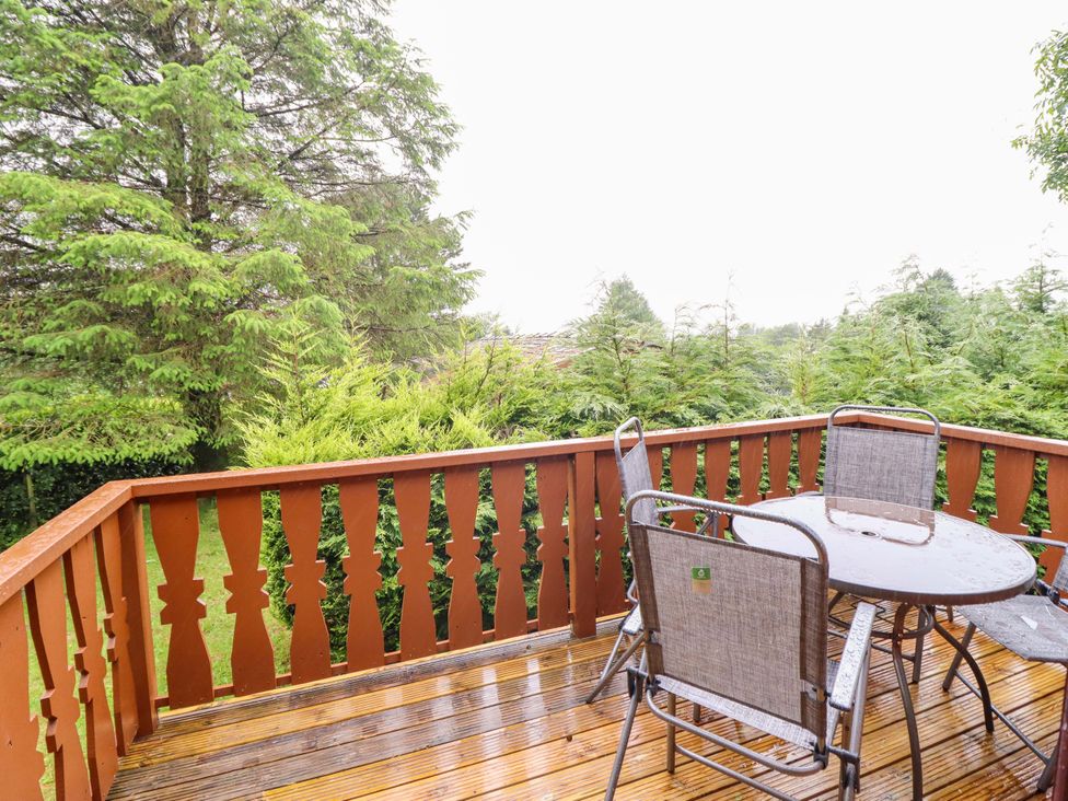 An outdoor area with a wooden deck, table, and chairs at Y Bwthyn Pren, Cabin 209, Trawsfynydd