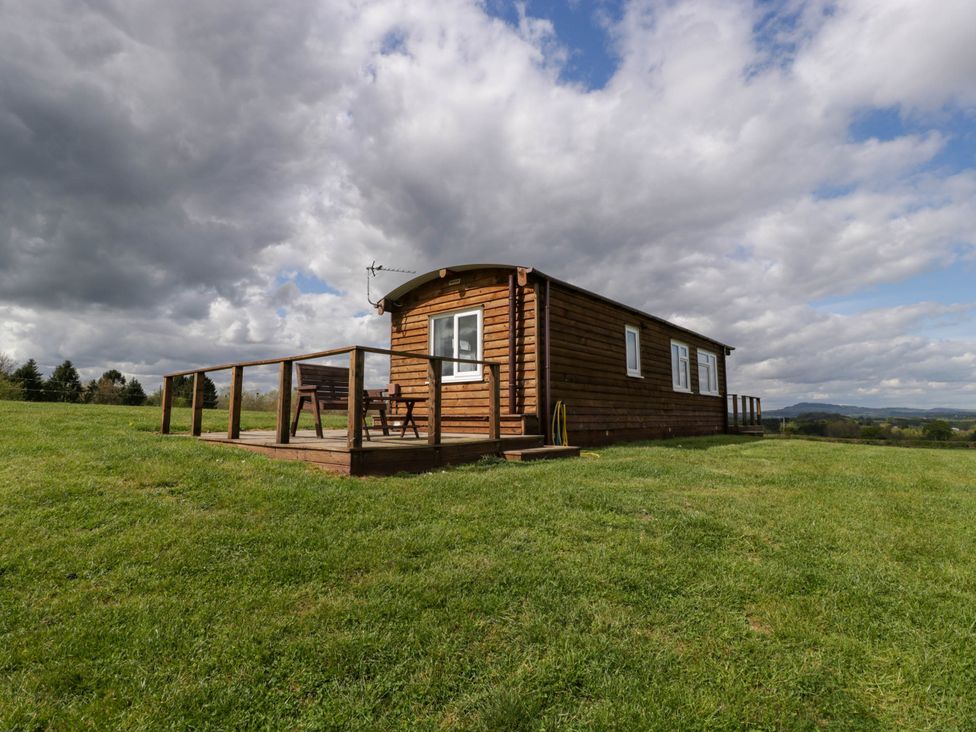 A wooden cabin with deck and bench in a grassy field under cloudy sky at Twilight in Raglan
