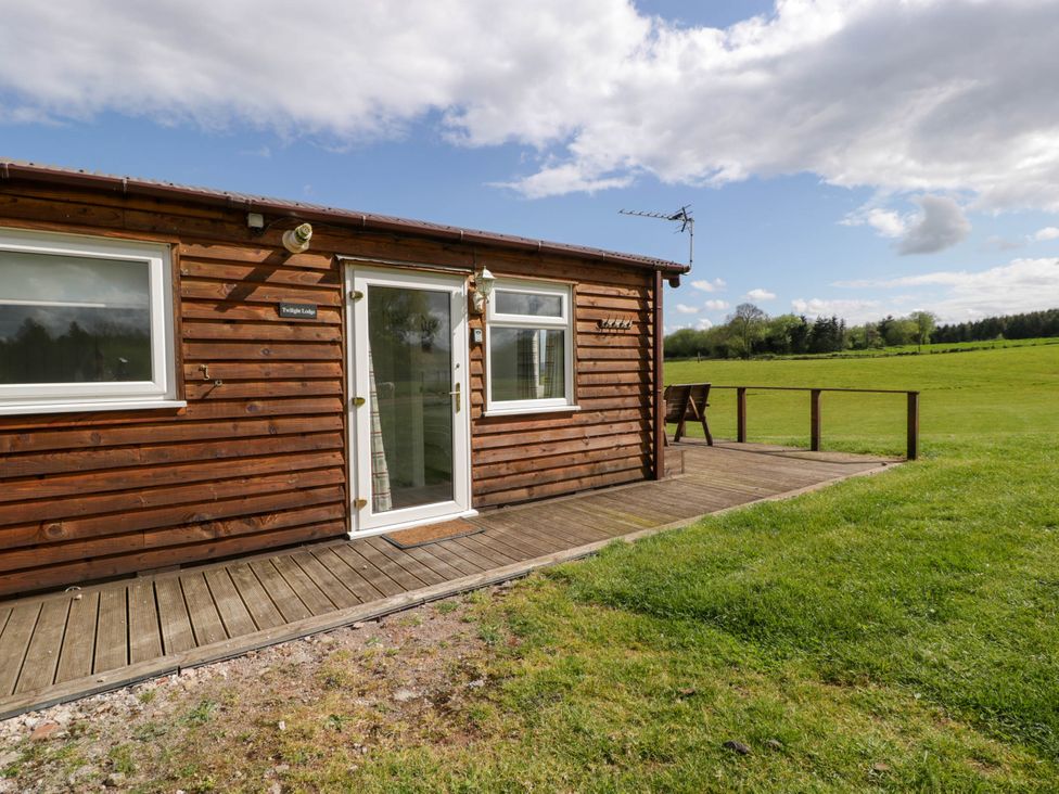 A wooden lodge with windows and a door opening onto a deck overlooking a grassy field at Twilight in Raglan