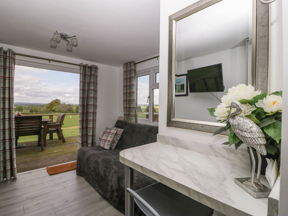 A living area with a black sofa and plaid pillows next to a marble table with a bird sculpture and flowers with windows and doors leading to an outdoor seating area at Twilight in Raglan