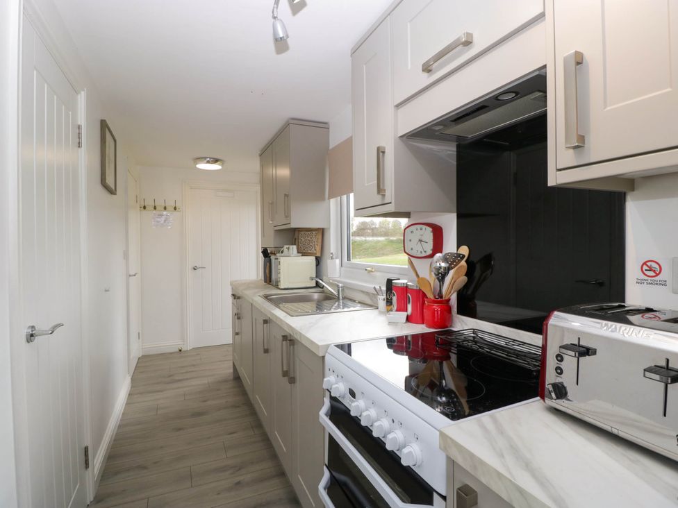 A kitchen with white cabinets a stove a toaster and kitchen utensils near a window at Twilight in Raglan