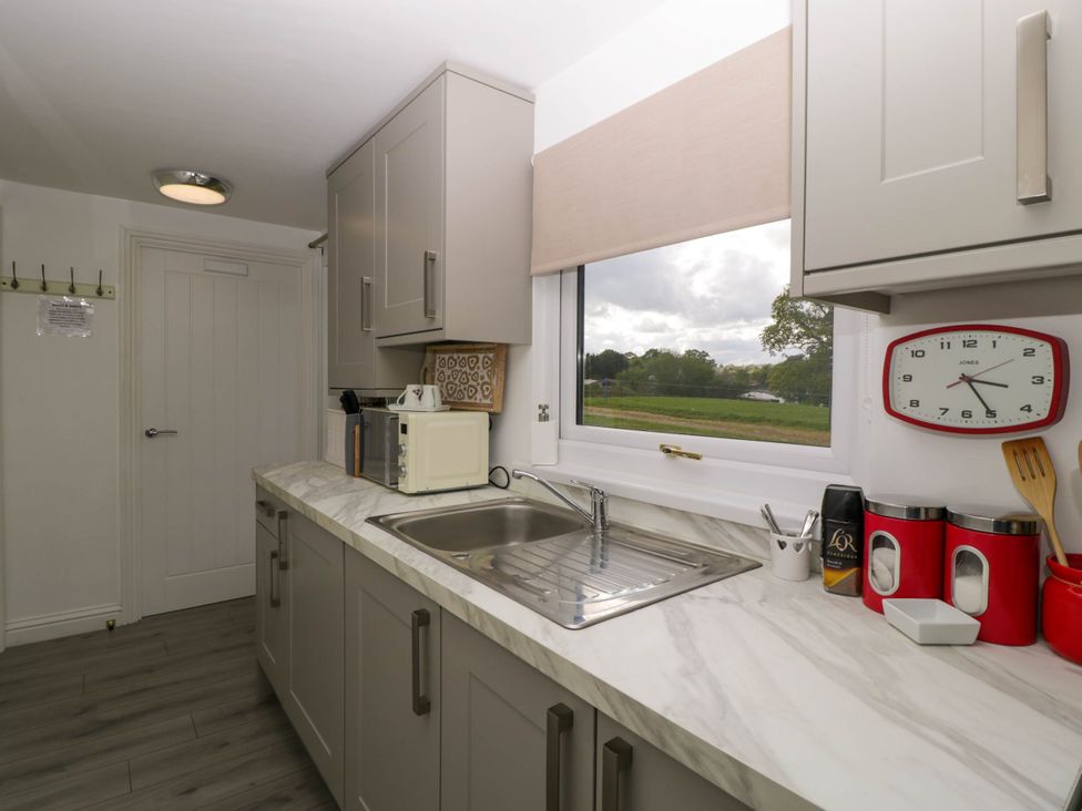A kitchen with a marble countertop, sink, microwave, wall clock, and window showing an outdoor view at Twilight in Raglan