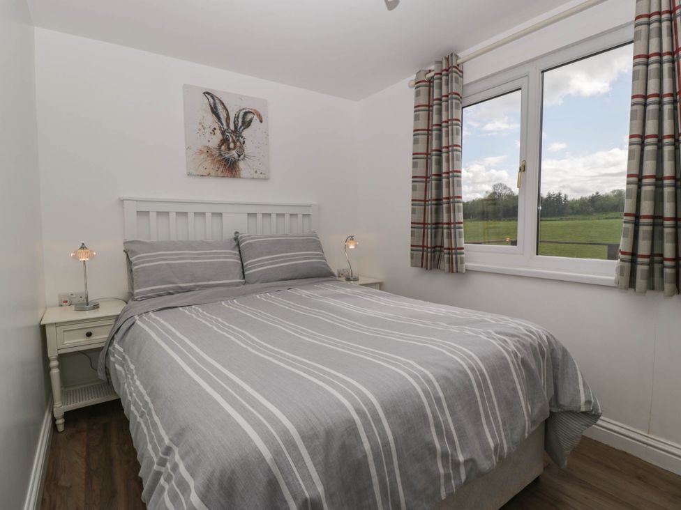 A bedroom with a double bed striped gray bedding bedside tables with lamps and a window with plaid curtains at Twilight in Raglan
