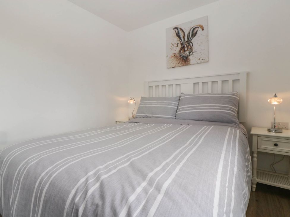 A bedroom with a bed with striped bedding two bedside tables with lamps and a hare painting above the bed at Twilight in Raglan
