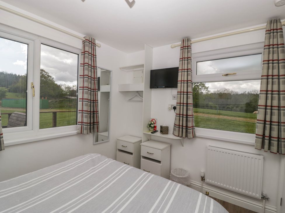 A bedroom with a bed a television two windows with checked curtains and two bedside tables at Twilight in Raglan