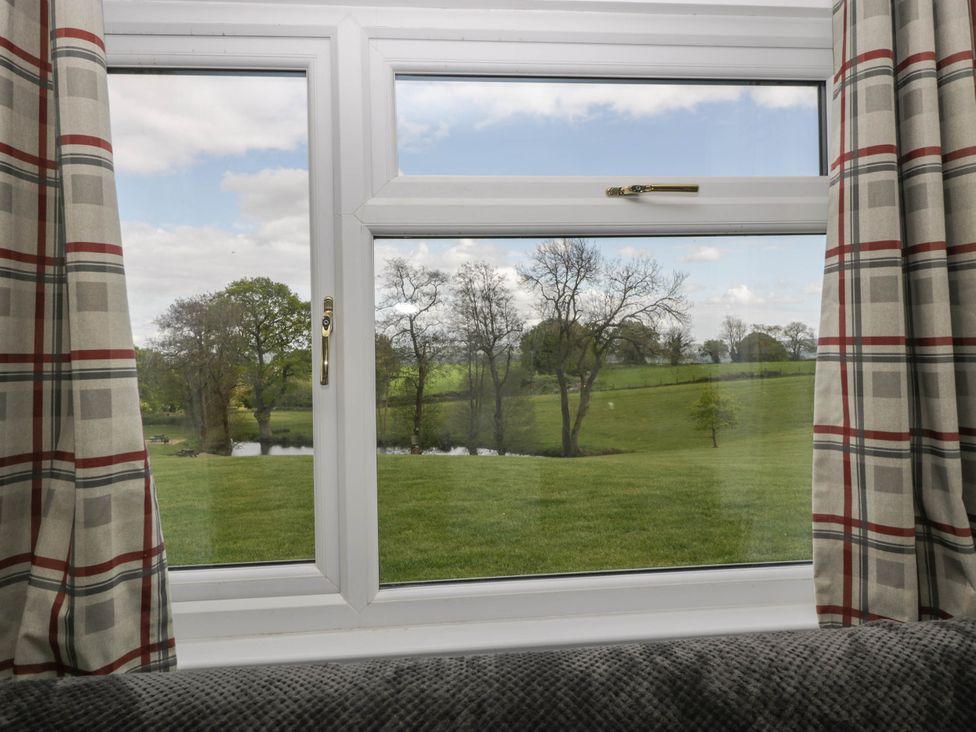 A window with plaid curtains looking out to a grassy field with trees and a pond at Twilight in Raglan