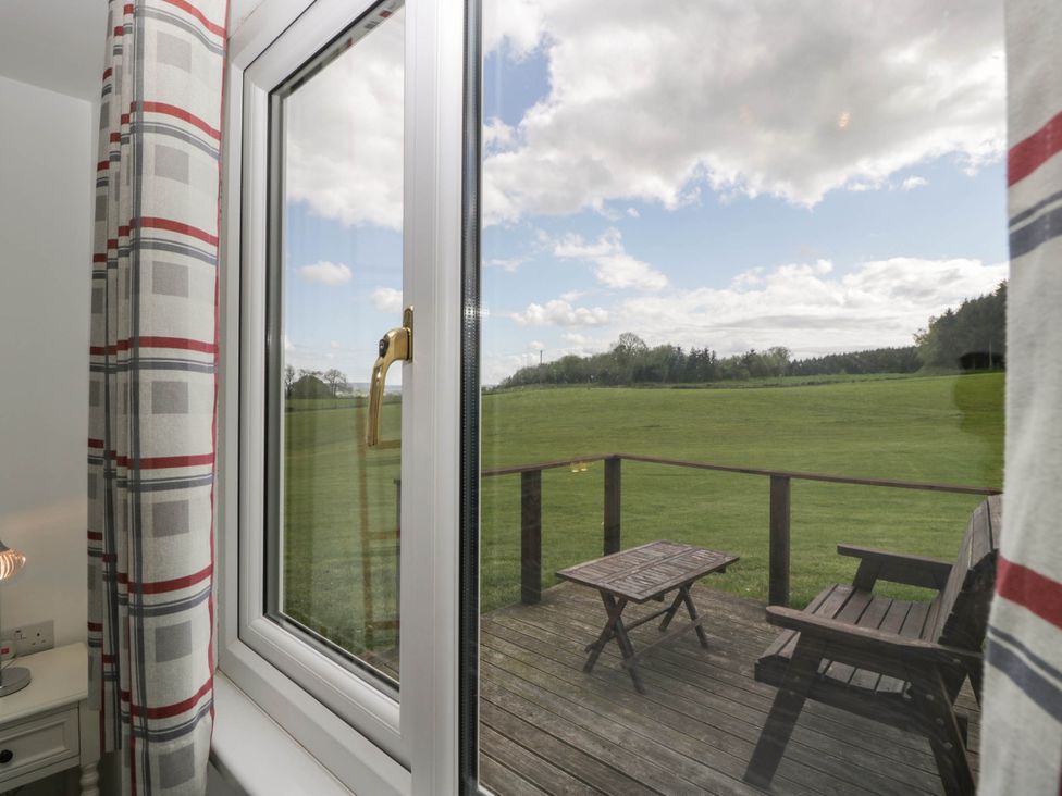 A window looking out to a wooden deck with a table and bench overlooking a grassy field at Twilight in Raglan