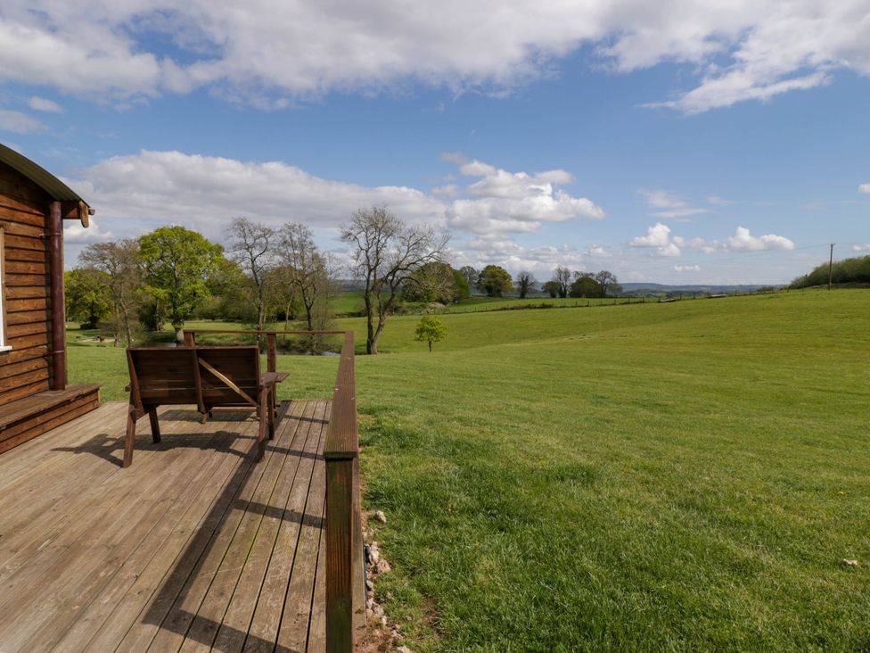 A wooden deck with a bench beside a wooden building overlooking a grassy field and trees at Twilight in Raglan