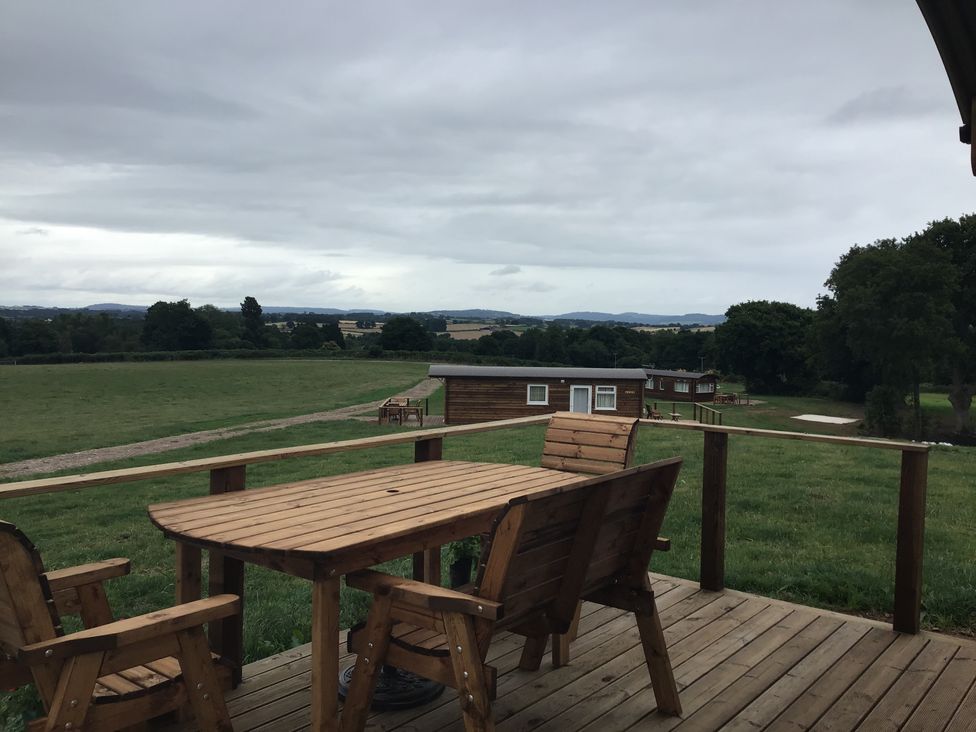 A wooden table and chairs on a deck overlooking cabins and fields at Twilight in Raglan