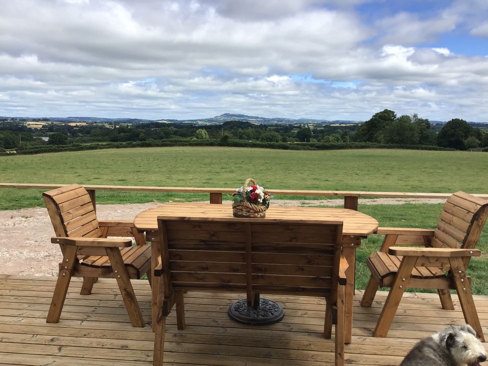 A wooden table with chairs on a deck overlooking a grassy field with a basket of flowers on the table at Twilight in Raglan