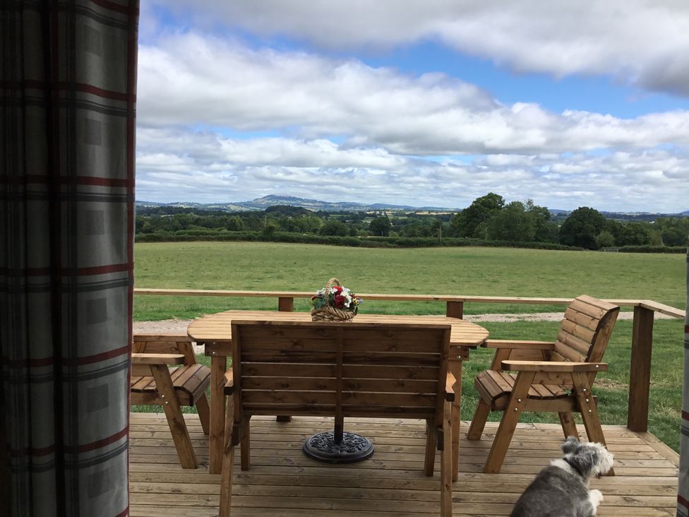 A wooden deck with a table and chairs overlooking a grassy field with trees and hills in the distance at Twilight in Raglan