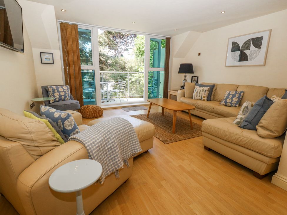 A living room with beige sofas a wooden coffee table and a glass door leading to a balcony at 6 Red Sails in Sandbanks