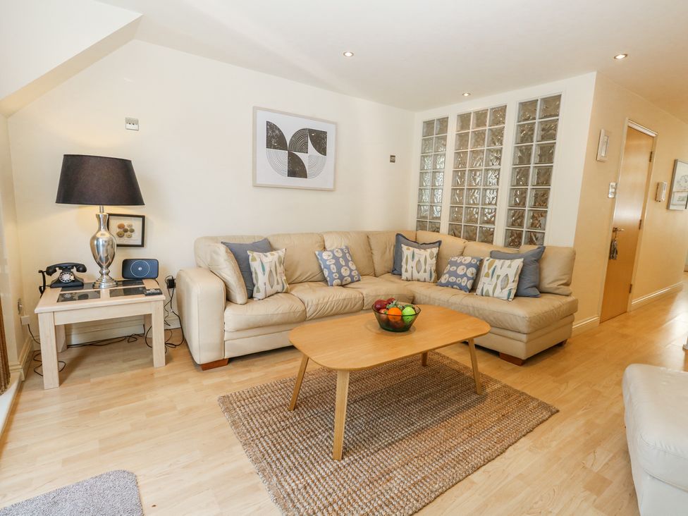 A living room with a beige sectional sofa and patterned cushions a wooden coffee table with a bowl of fruit a table lamp and vintage telephone on a side table at 6 Red Sails in Sandbanks