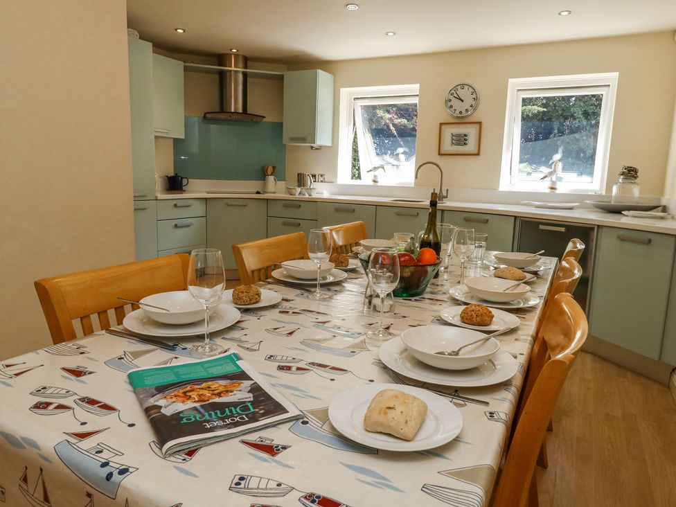 A kitchen with a dining table set with plates bowls bread wine glasses and a cookbook at 6 Red Sails in Sandbanks