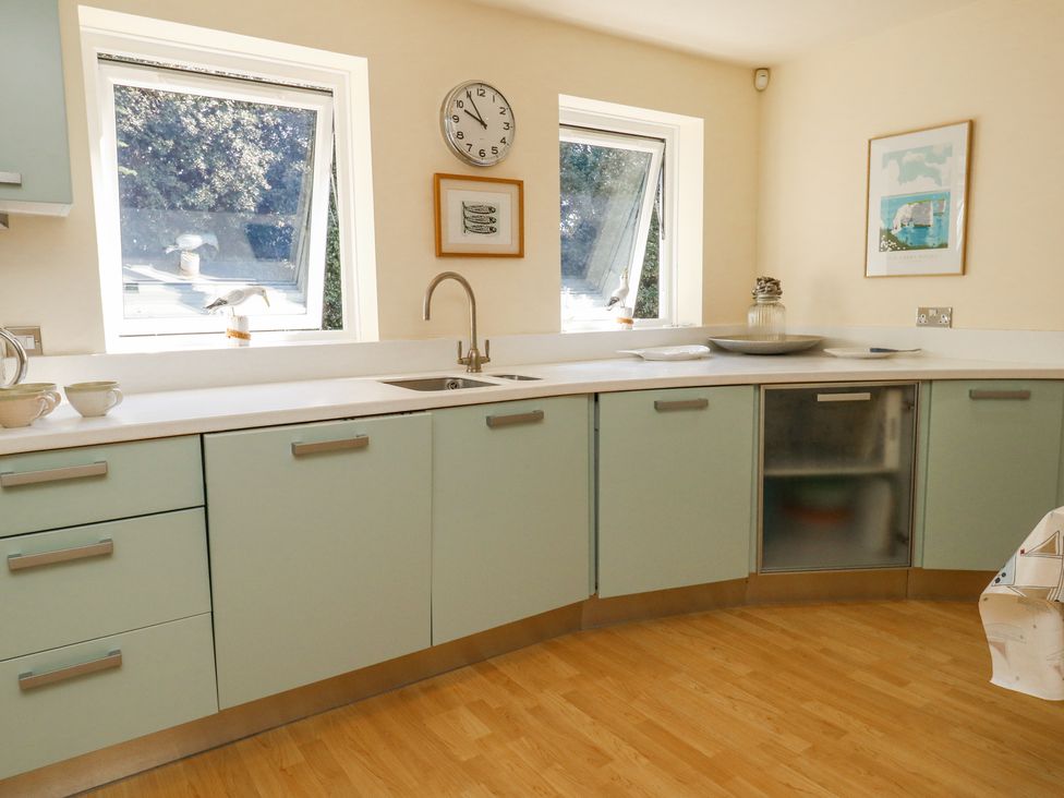 A kitchen with green cabinets white countertops two windows a sink a wall clock and framed pictures at 6 Red Sails in Sandbanks